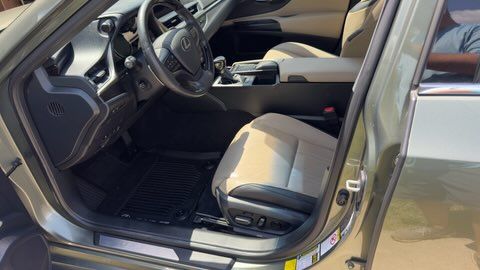 Open car door showing beige leather interior, dashboard, steering wheel, and front seat