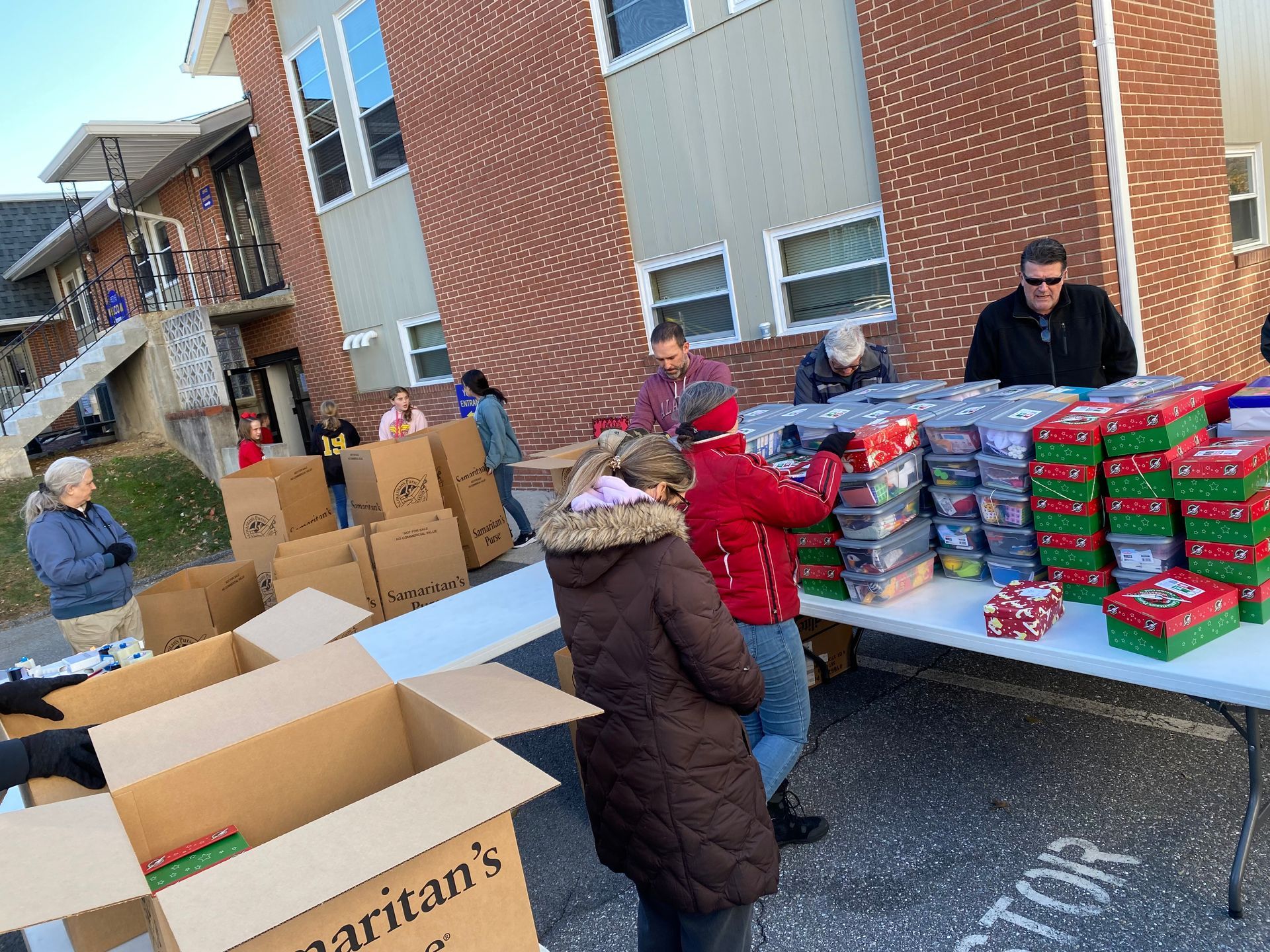 A woman wearing a mask is giving away bottles of water in a cardboard box at a Bethel Baptist Church missions event.