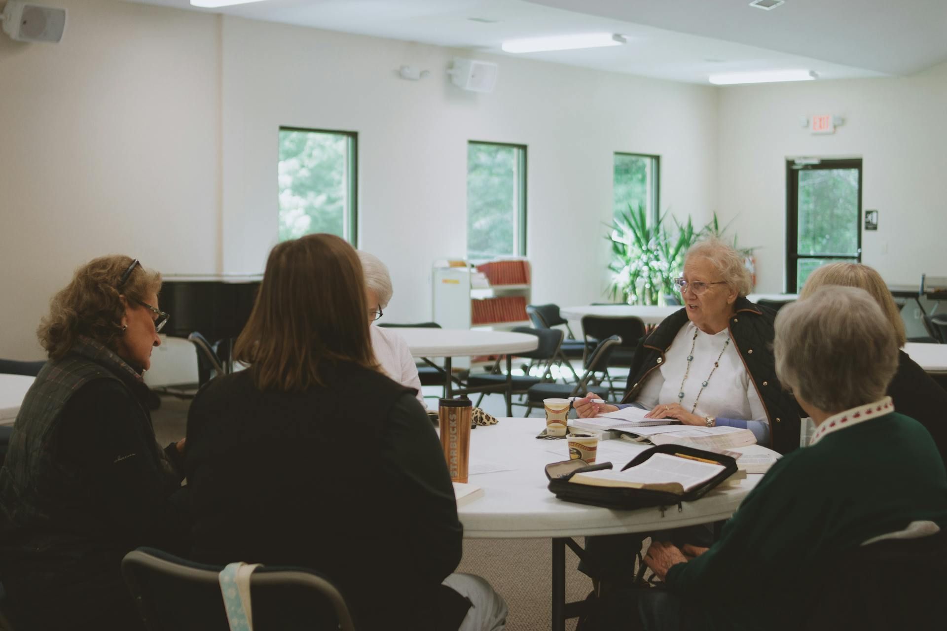 A group of people sit around a circular table in a brightly lit room for a discussion or meeting.