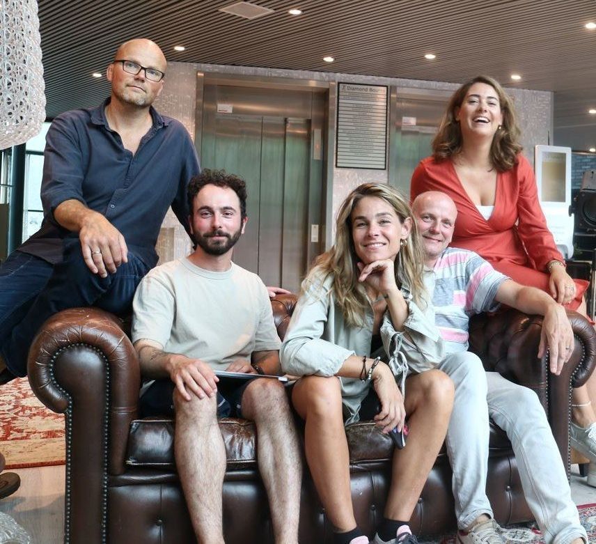 Vijf lachende mensen zitten op een leren bank in een moderne lounge.