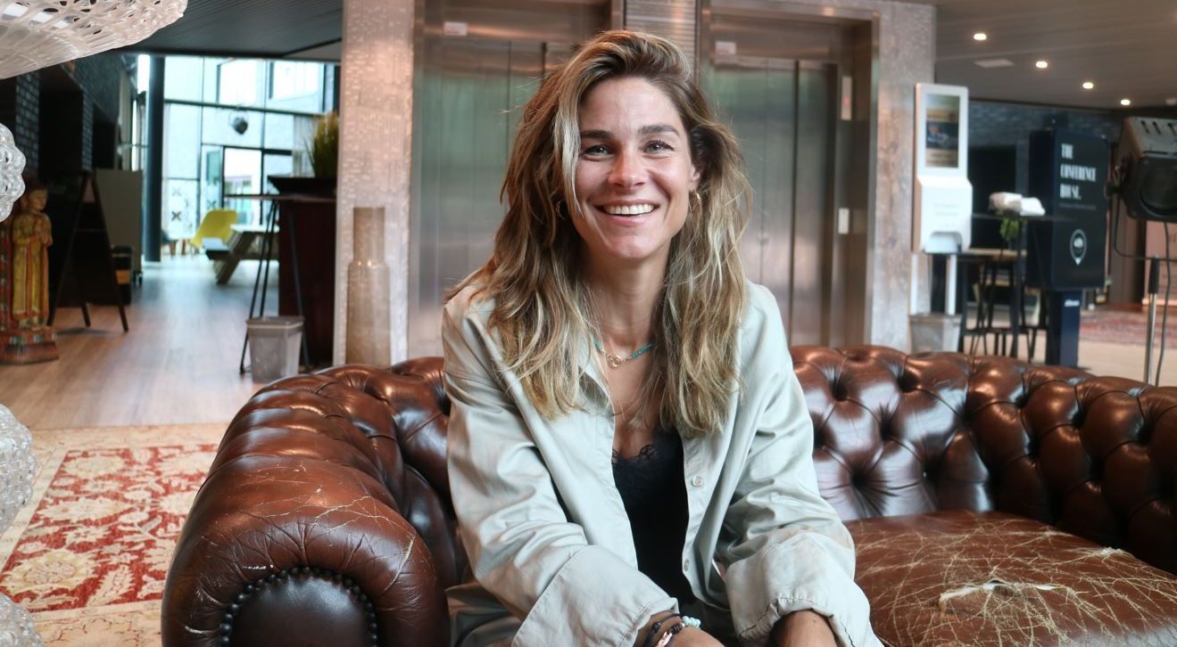 Een lachende vrouw zit op een bruine leren bank in een moderne lobby.