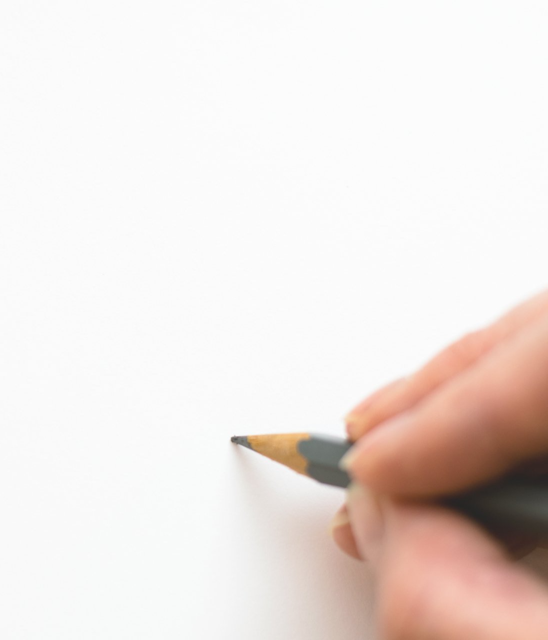 Hand met een geslepen potlood boven een blanco wit vel papier.