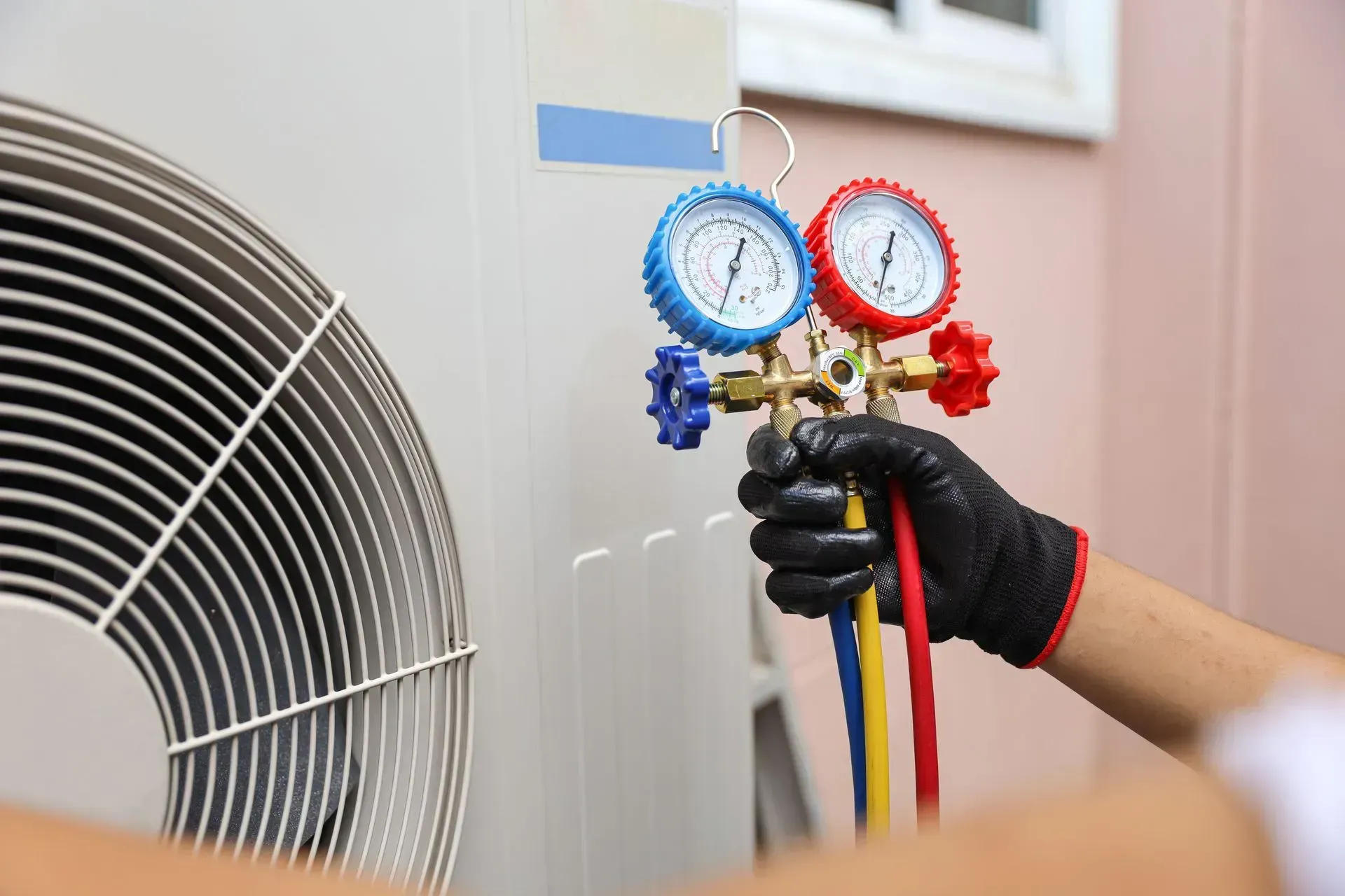 Technician holding HVAC manifold gauges beside an outdoor AC unit