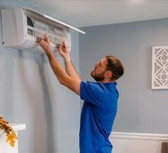 Man installing a white window air conditioner in a light blue room