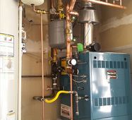 Mechanical equipment in a utility room, with pipes, gauges, and a blue furnace unit.