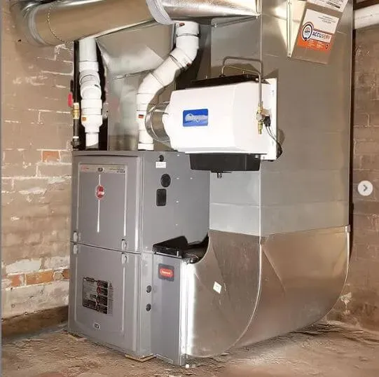 Basement HVAC and furnace with ductwork and vent pipes beside a brick wall