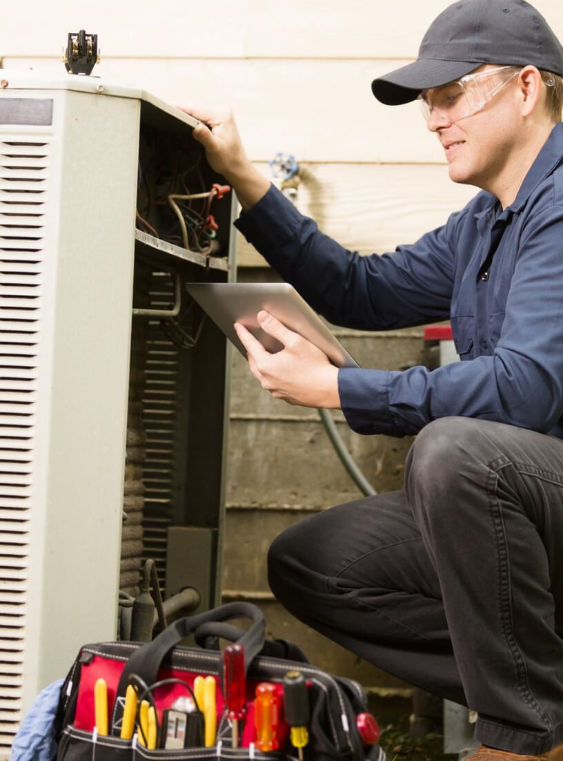 Technician inspecting an outdoor HVAC unit with tools in a carrying bag.