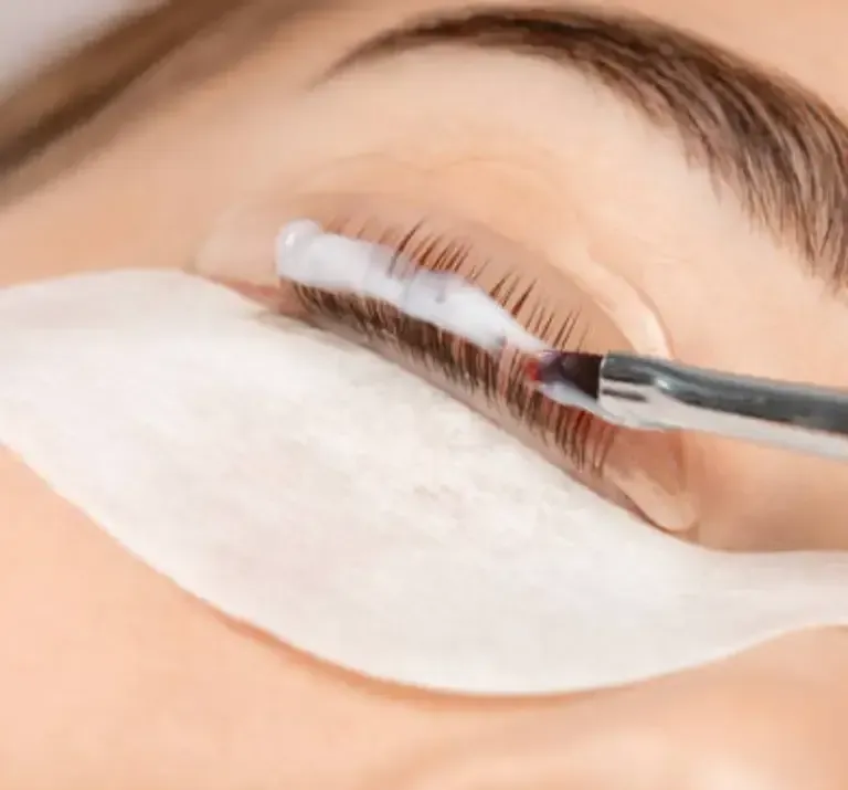 Eyelash extension being applied with tweezers on a closed eye, with white under-eye pads.