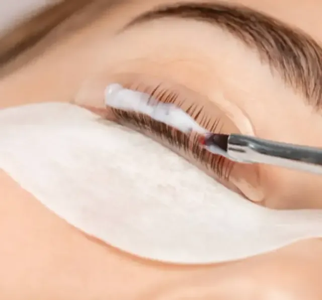 Close-up of eyelash extension application with tweezers and eye patches