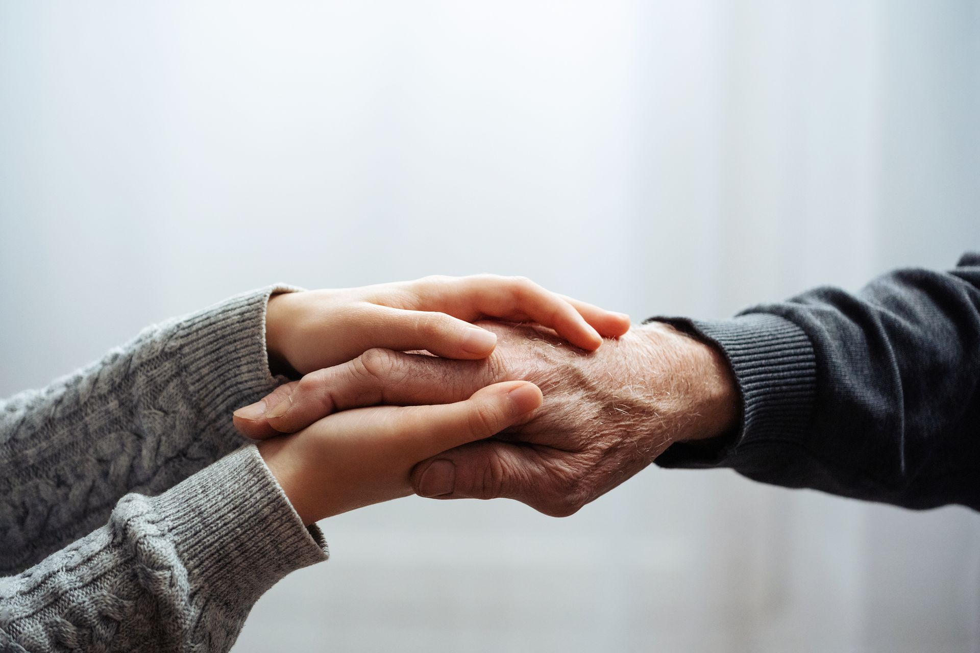 Two hands, one older and one younger, clasped together, suggesting comfort and support.