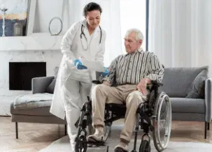 Woman in wheelchair smiles at caregiver in hallway, arms around shoulders.
