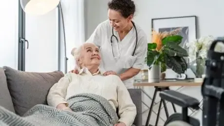 Caregiver comforts senior in living room. Both smile.