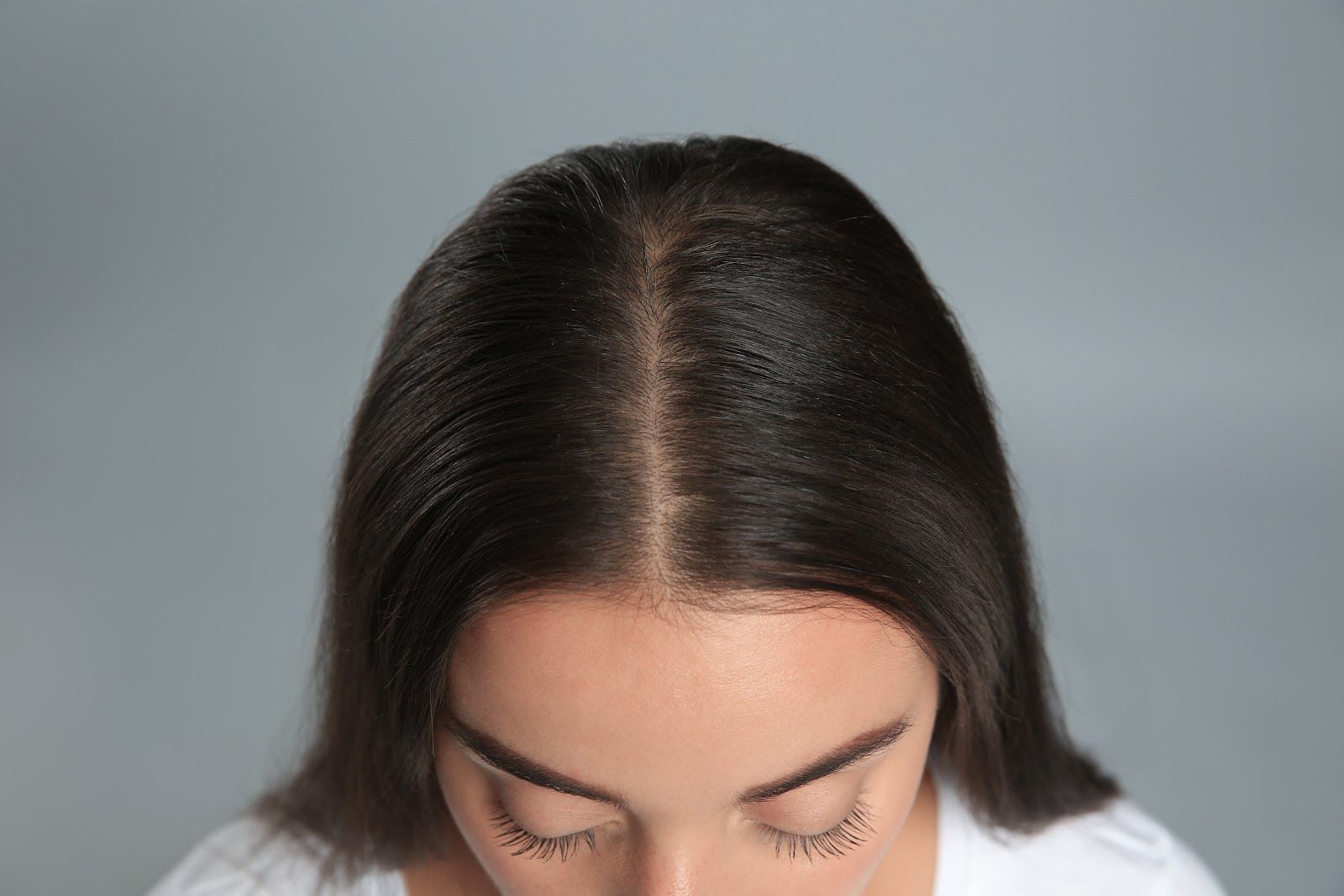 Person with dark hair looking downward against a plain gray background