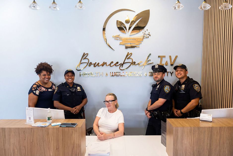 Five people stand behind a wooden reception desk in front of a wall sign that reads