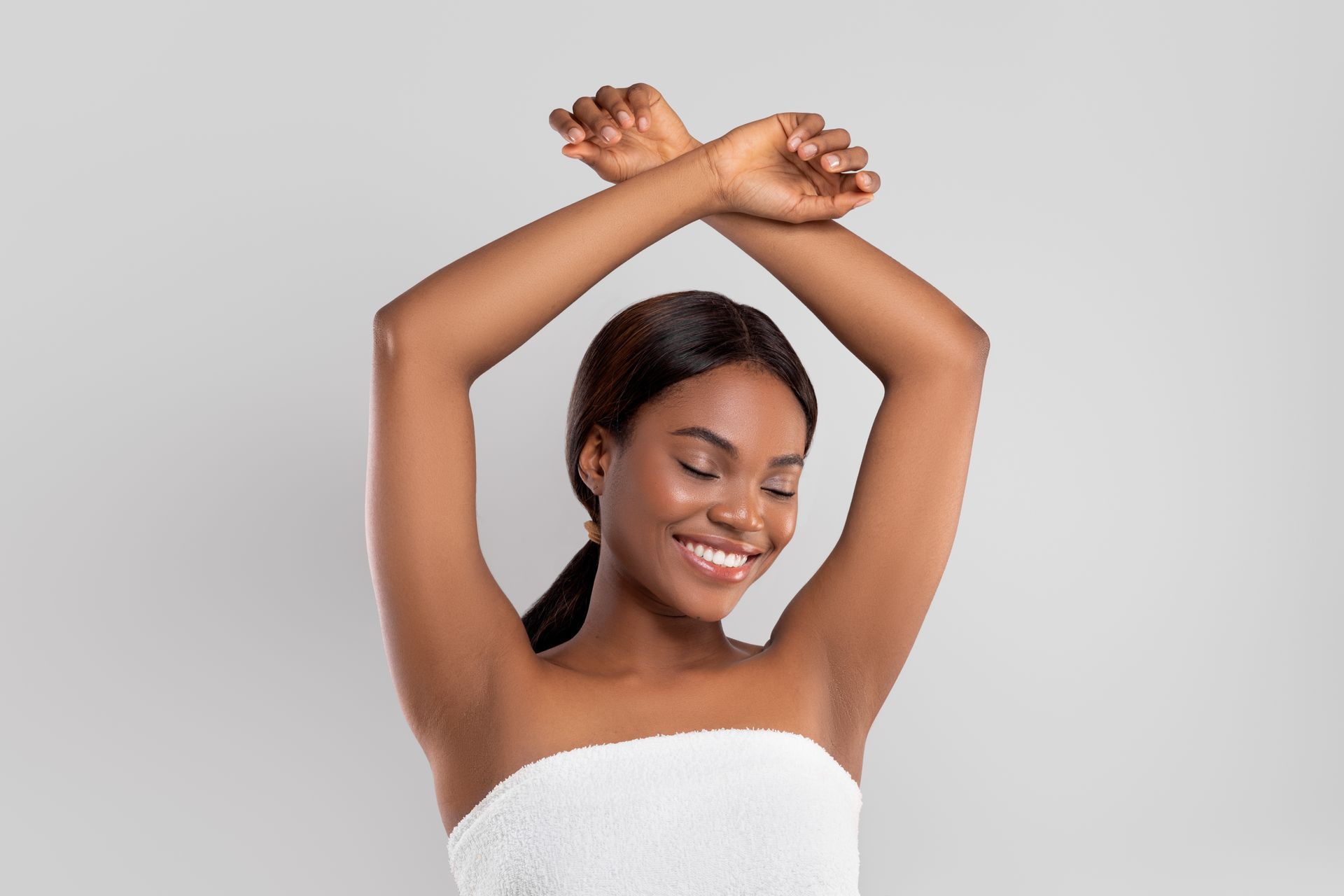 A woman wrapped in a white towel is smiling with her arms in the air.