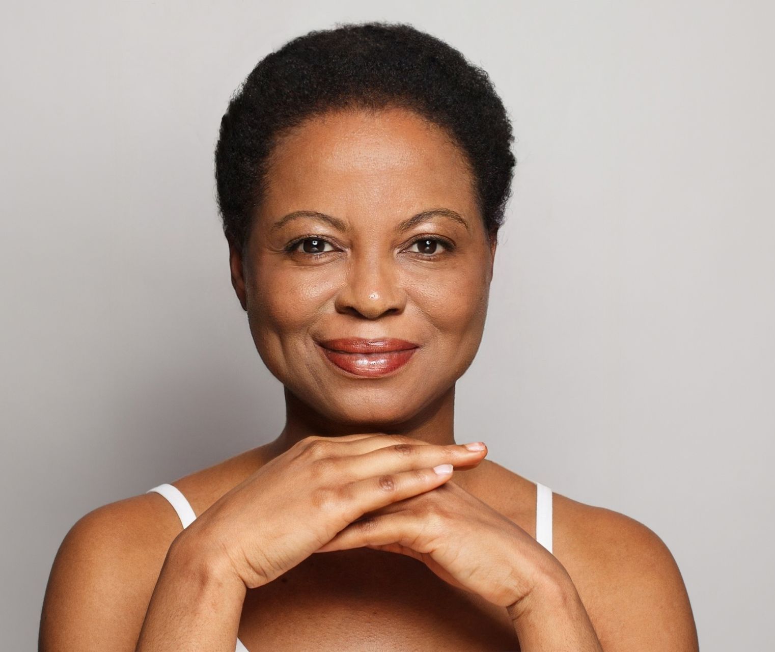 A woman is smiling with her hands on her face.