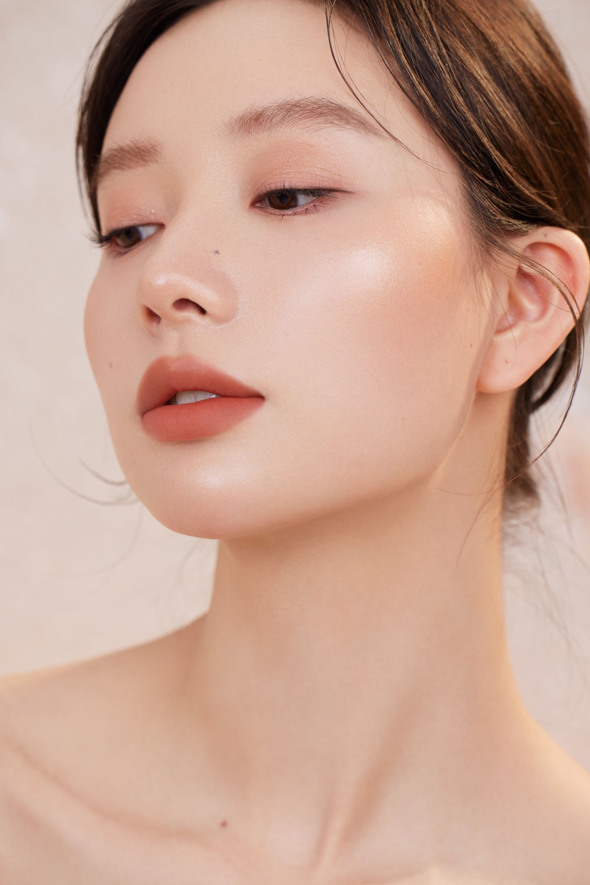 Close-up portrait of a person with soft makeup, looking left against a light background