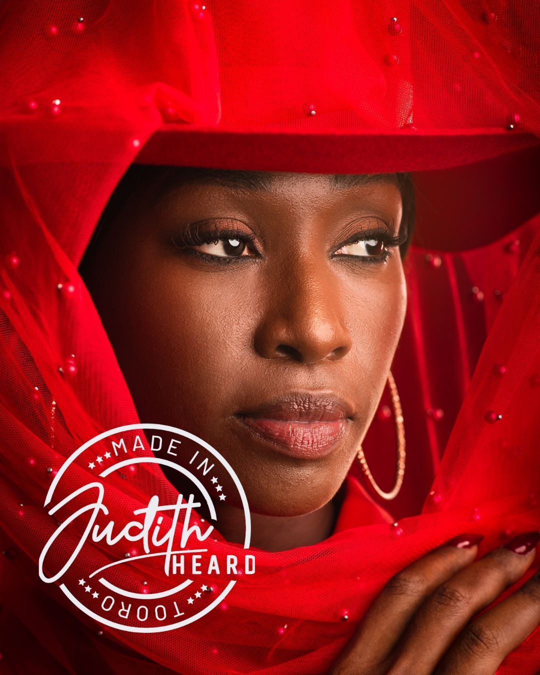 Portrait of a woman in a red hat and veil, with a “Made in Judith Heard” logo