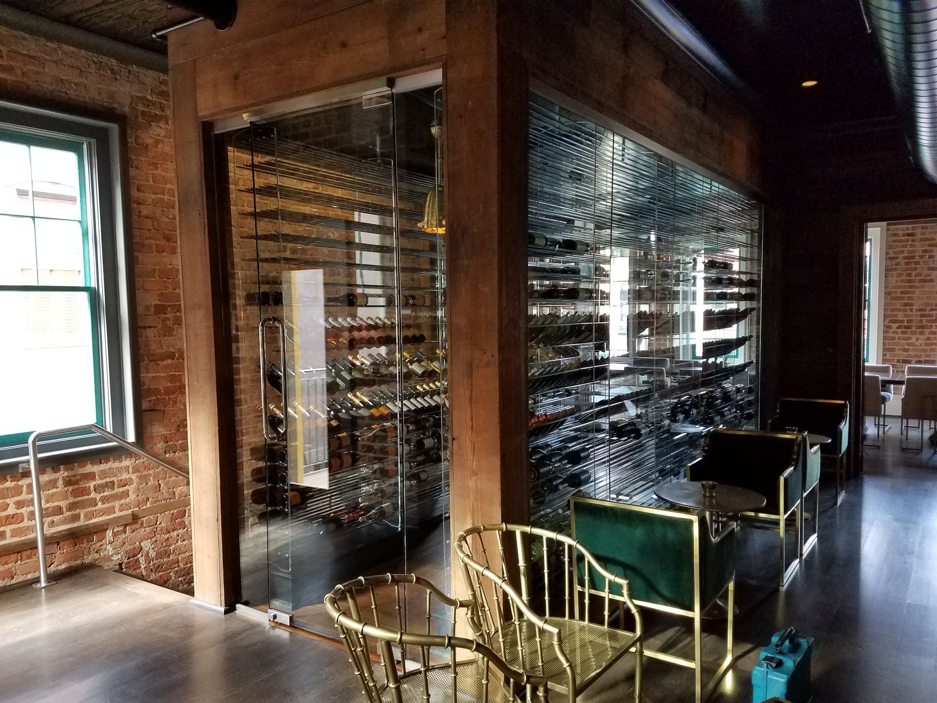 Wood-paneled wine cellar with glass walls, wine racks, and chairs beside a sunlit window