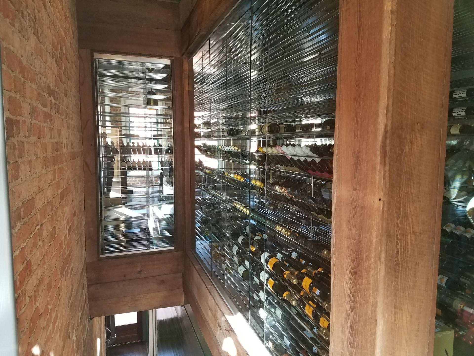 Wine cellar with wooden racks and glass doors, filled with bottles on both sides.