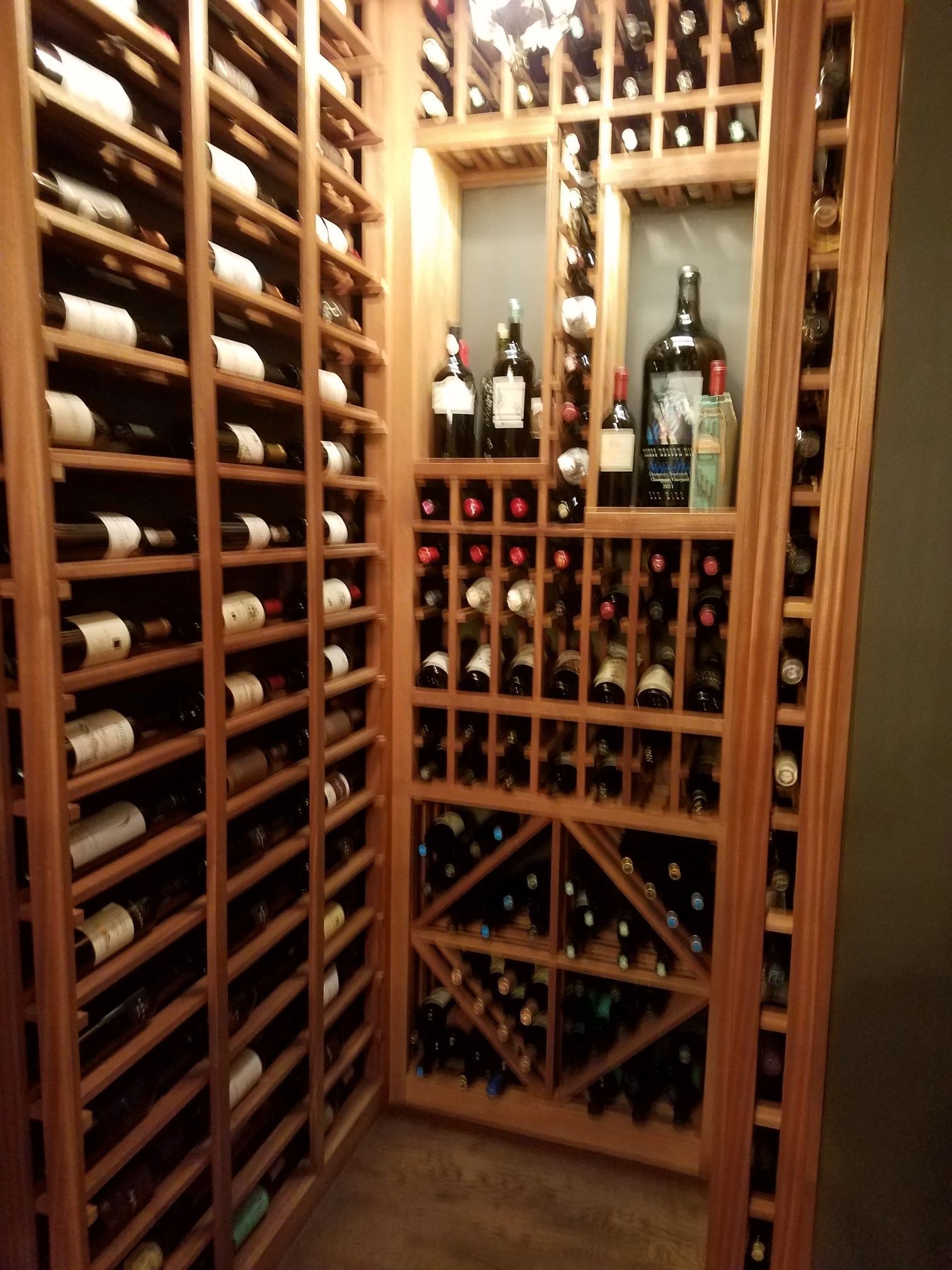 Wine cellar with wooden racks holding bottles on three sides, warmly lit and organized.