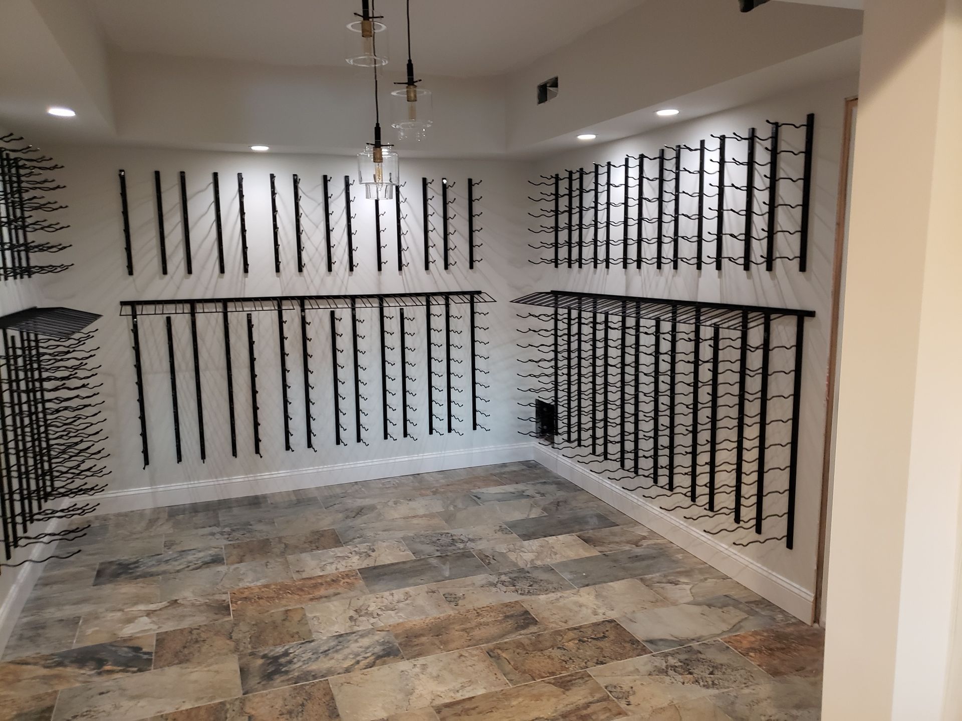 Interior of a walk-in closet with white walls, black shelving rods, and tiled floor under ceiling lights