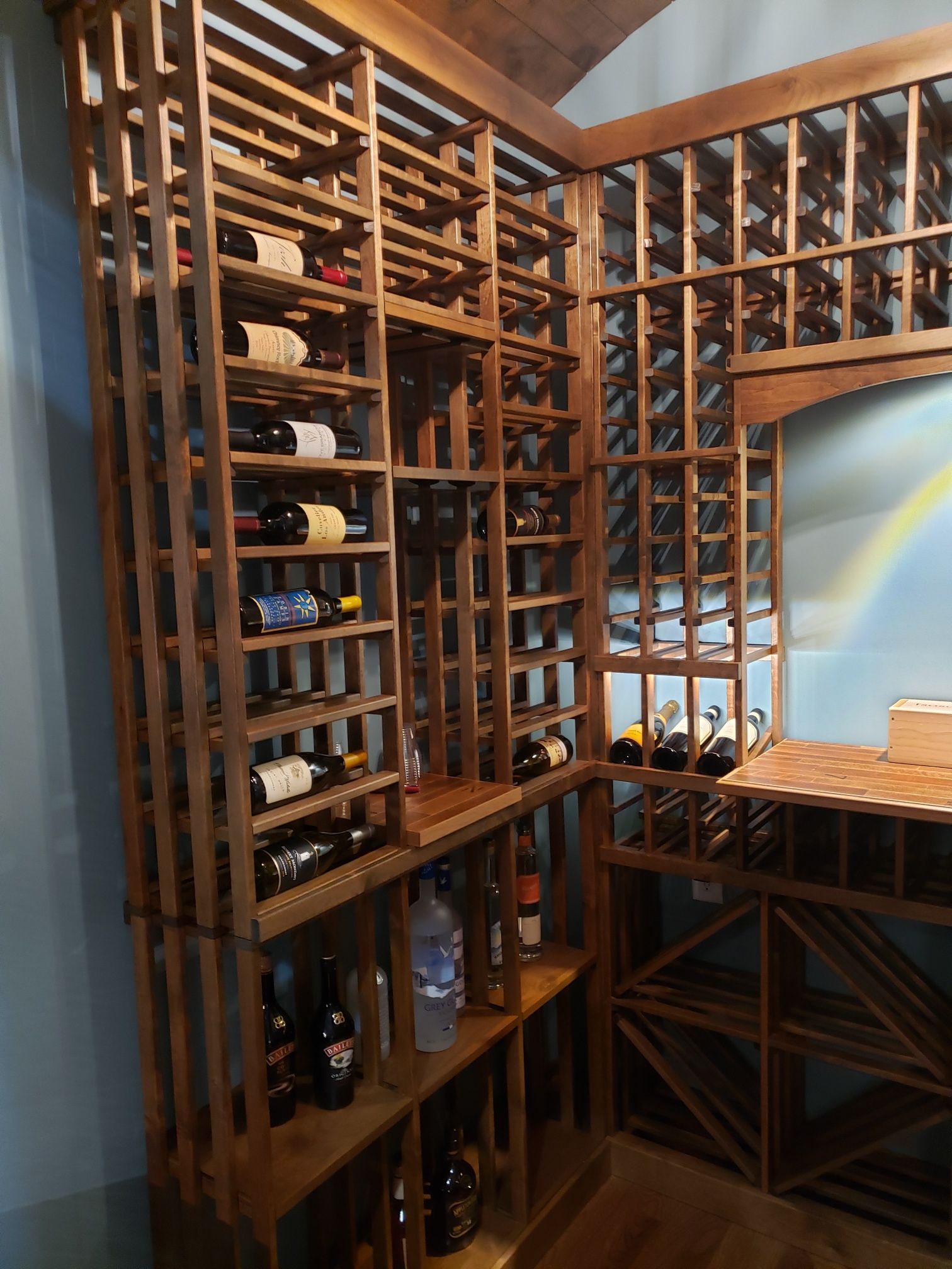 Wooden wine cellar shelves filled with bottles beside a rainbow-painted wall and wooden counter.