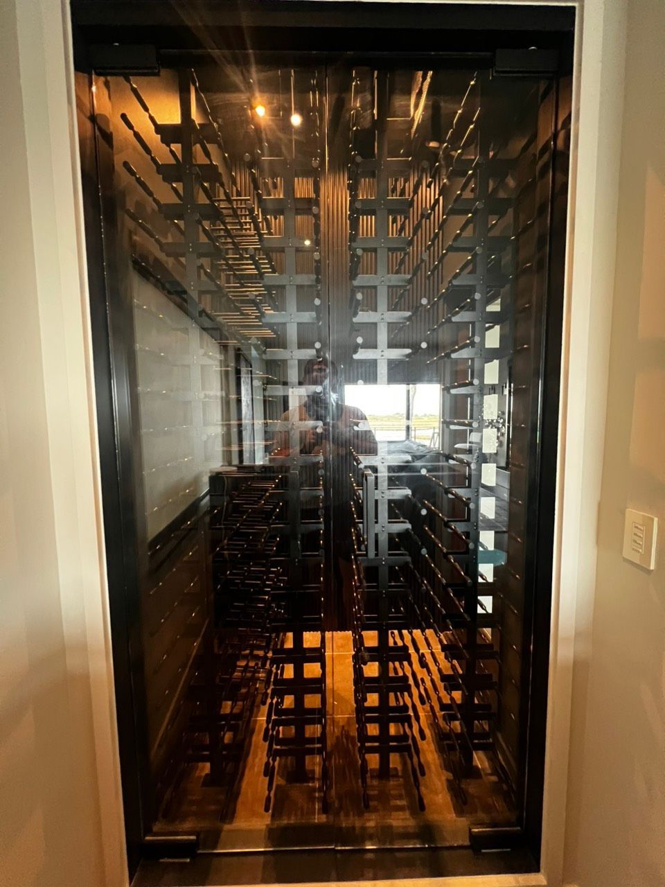 Tall glass-door wine cooler filled with empty racks in a dimly lit kitchen or bar area