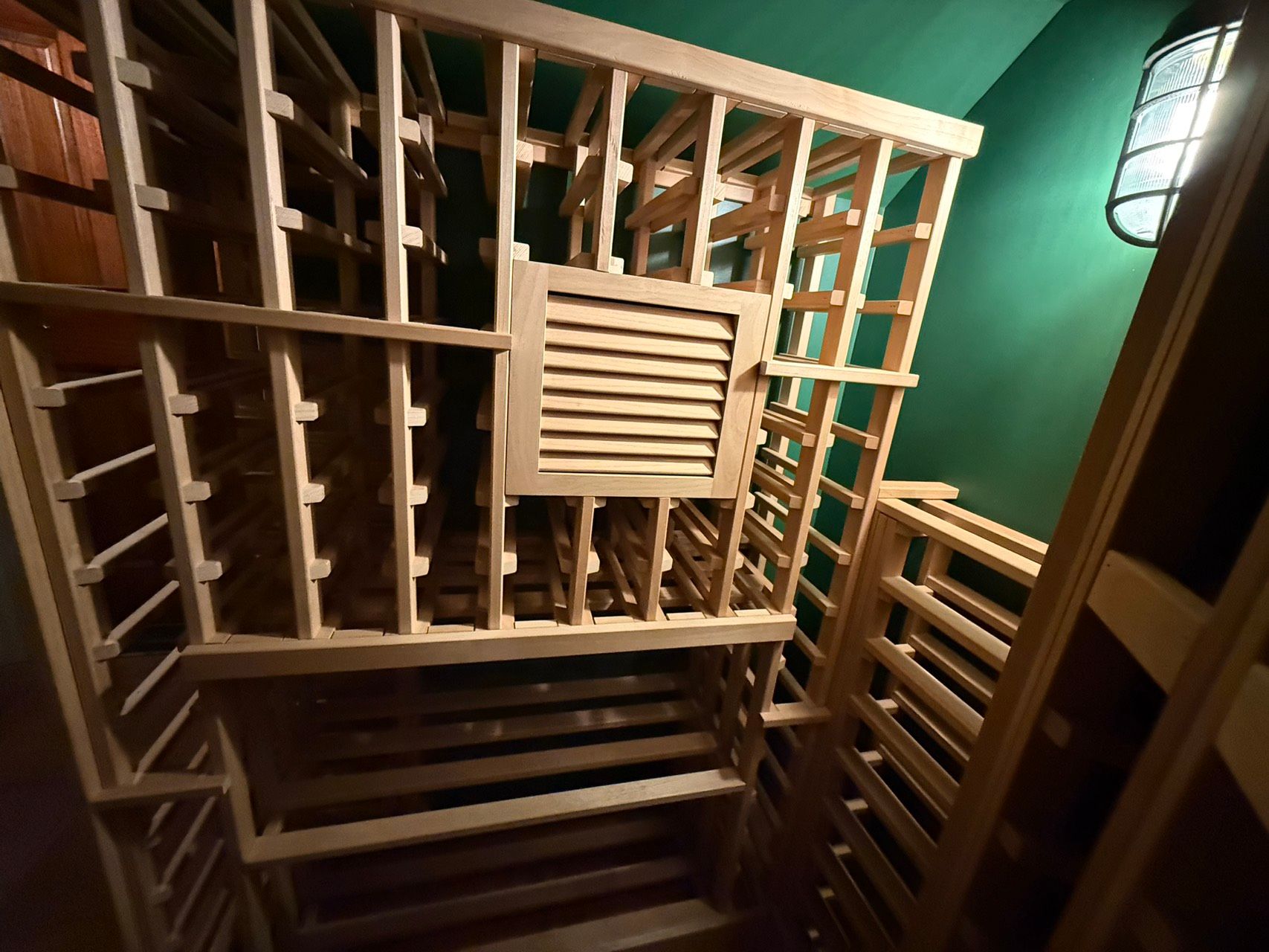 Wooden wine rack against a green wall in a dimly lit stairwell or cellar.