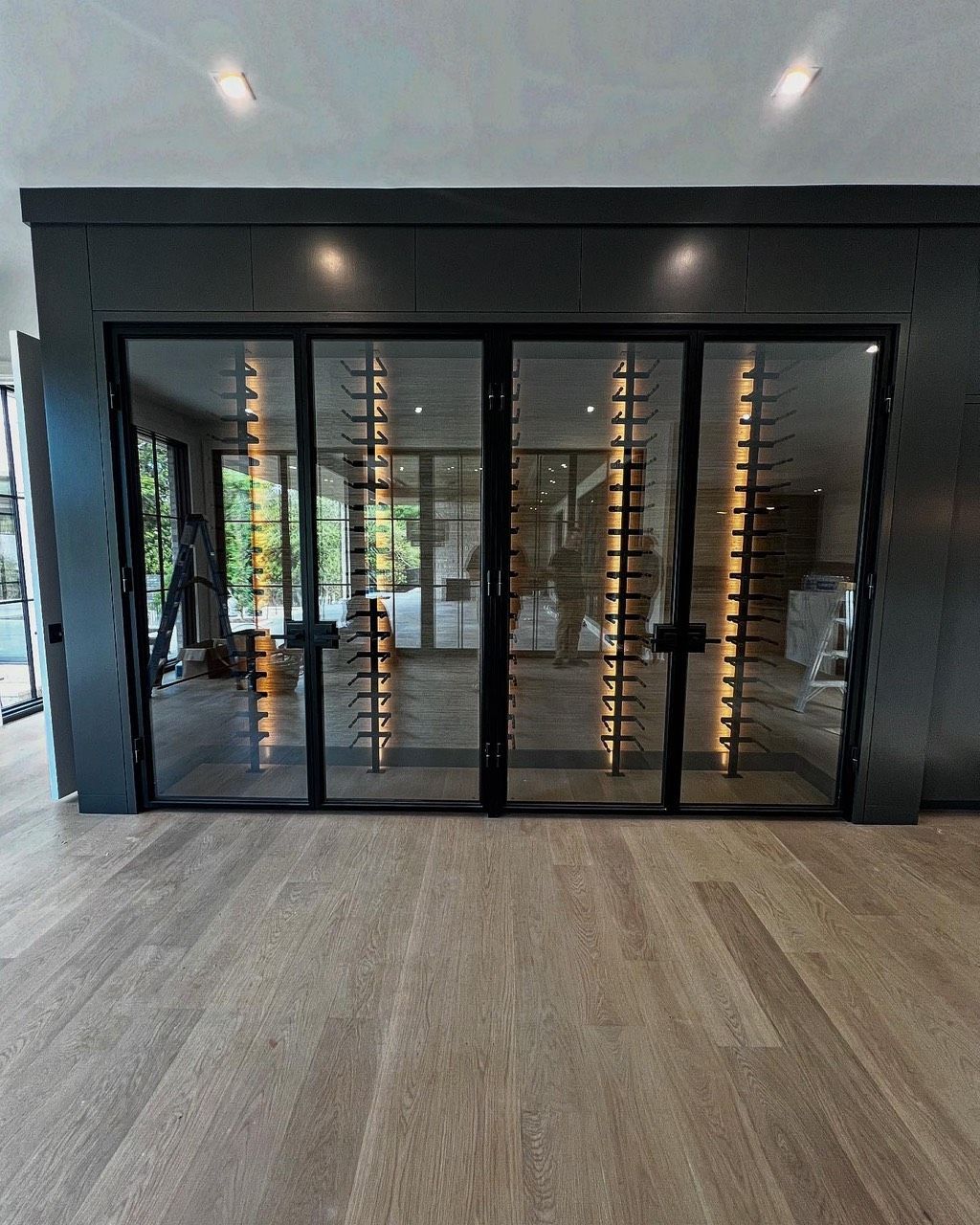 Modern interior with black-framed glass folding doors and light wood flooring.