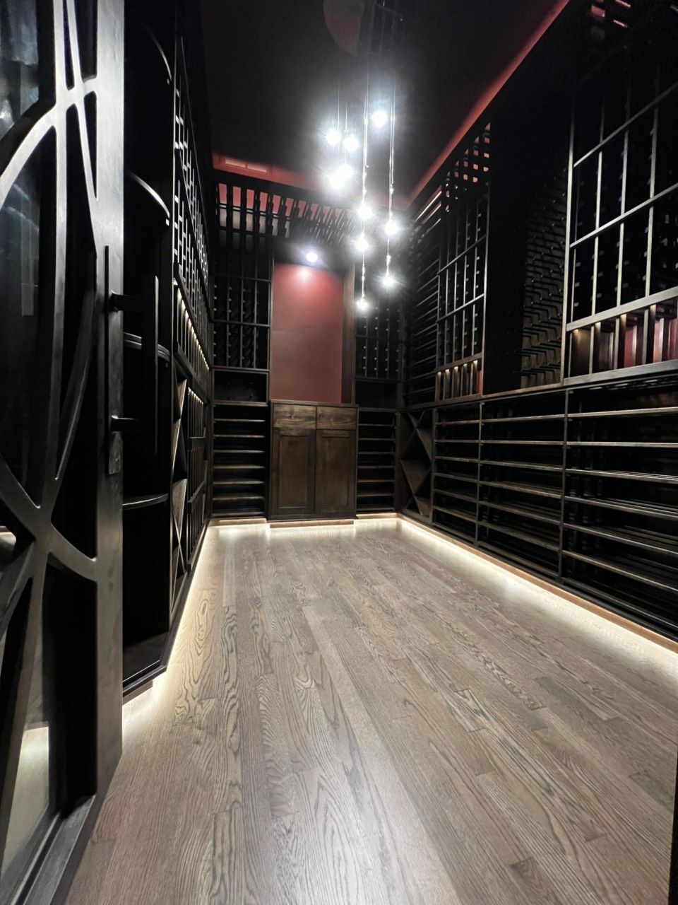 Dimly lit narrow hallway with black walls, wooden floor, and stairs at the far end