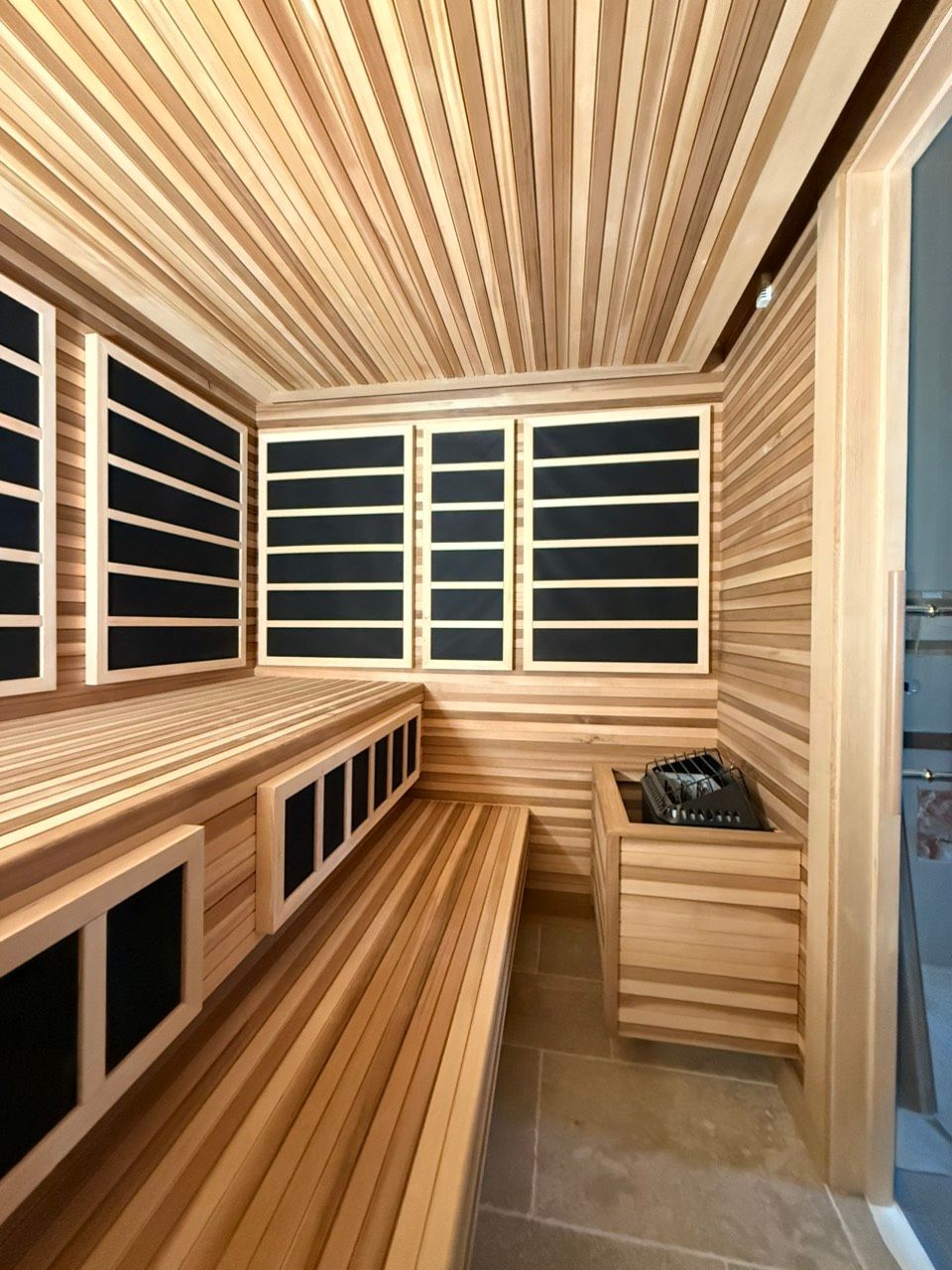 Wood-paneled sauna with bench seating, black windows, and a wooden heater in the corner.