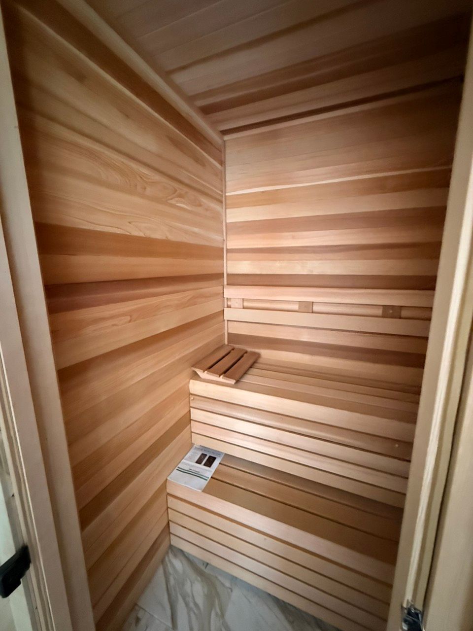 Wood-paneled sauna with tiered benches and a control panel inside a narrow corner room