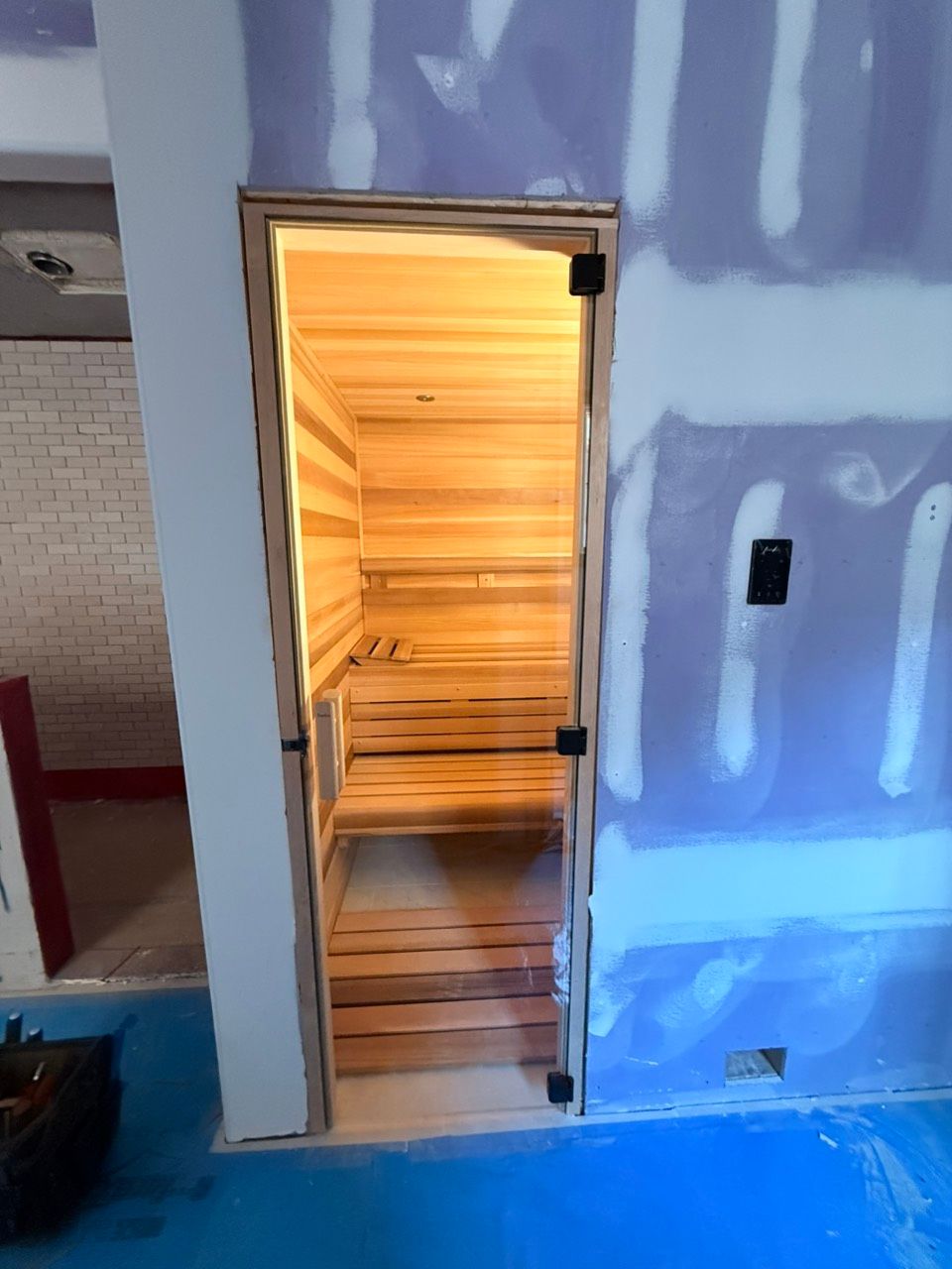 Open doorway to a warmly lit wooden sauna room in an unfinished interior wall.