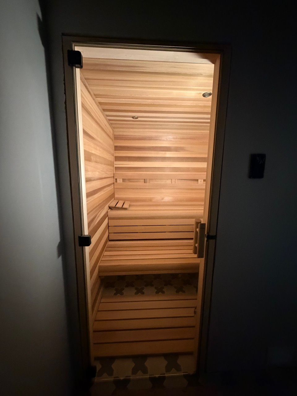 Wood-paneled sauna room glowing warm light, with benches and a heater inside.