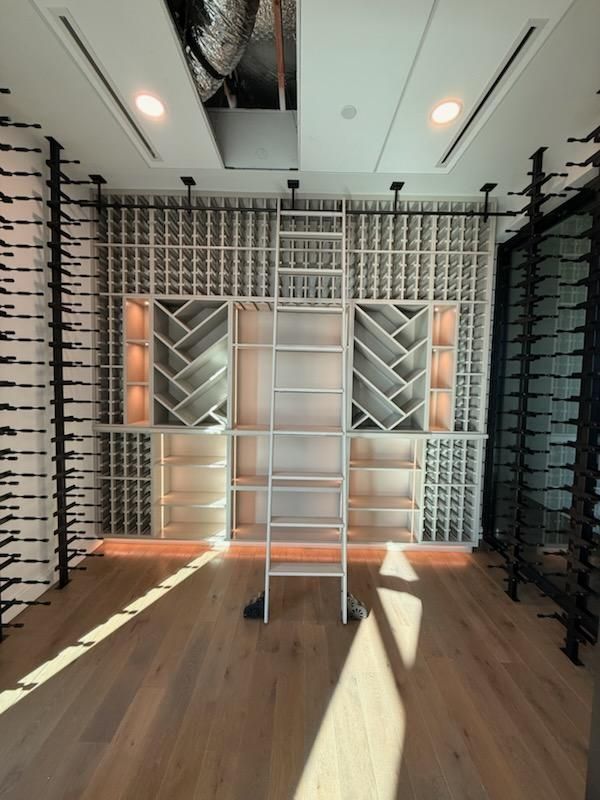Empty walk-in closet with built-in shelves, hanging rods, a ladder, and warm wood flooring.