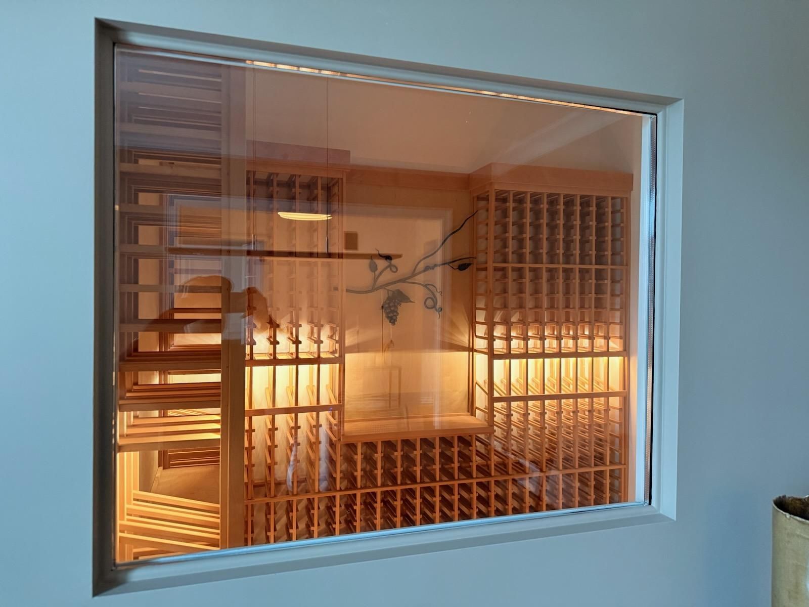 Modern interior seen through a window, with warm lighting and wooden shelving inside