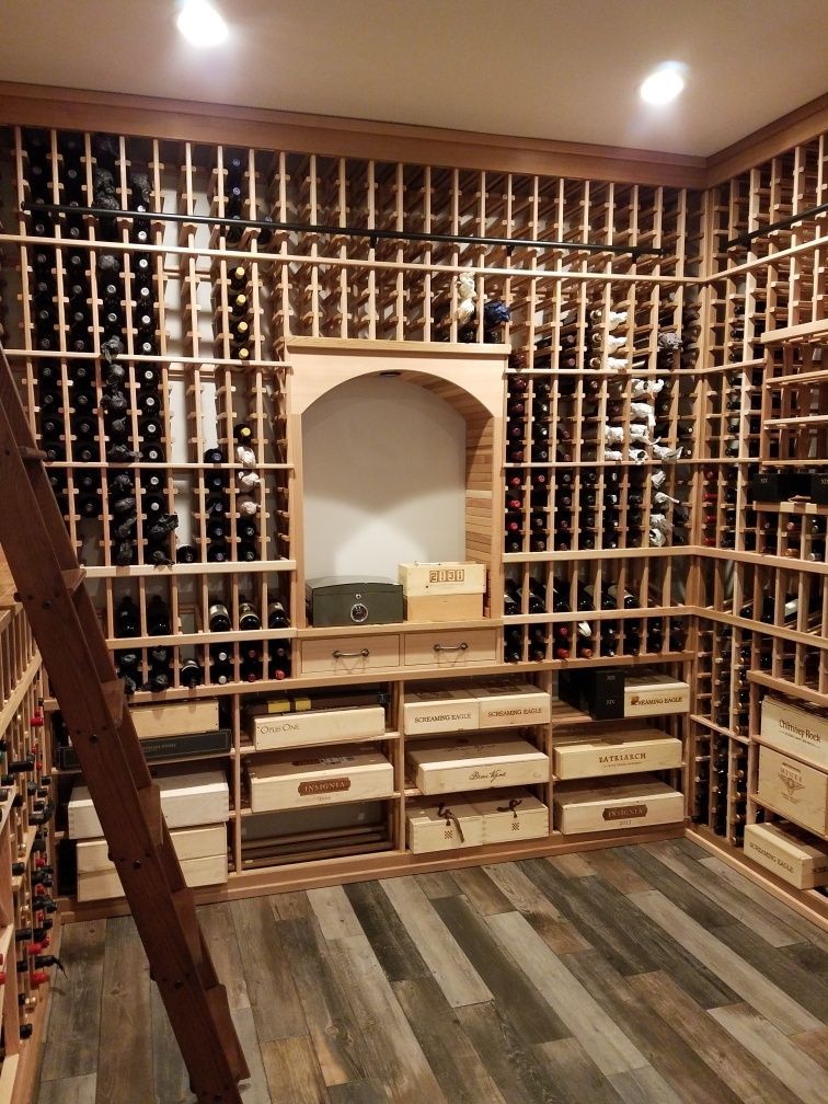 Wine cellar with floor-to-ceiling bottle racks, a central arch niche, and drawers beneath in warm wood tones