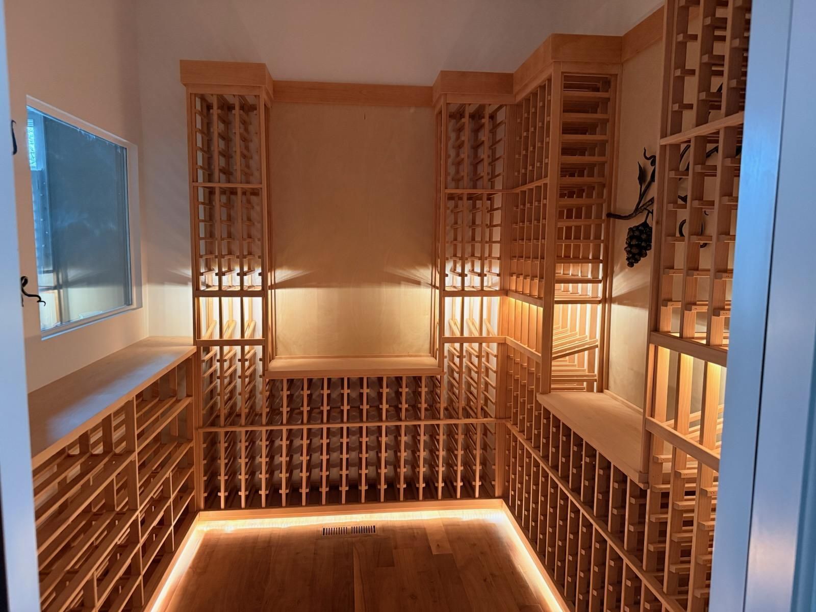 Warm-lit wooden wine cellar with floor-to-ceiling bottle racks and a small central bench seat