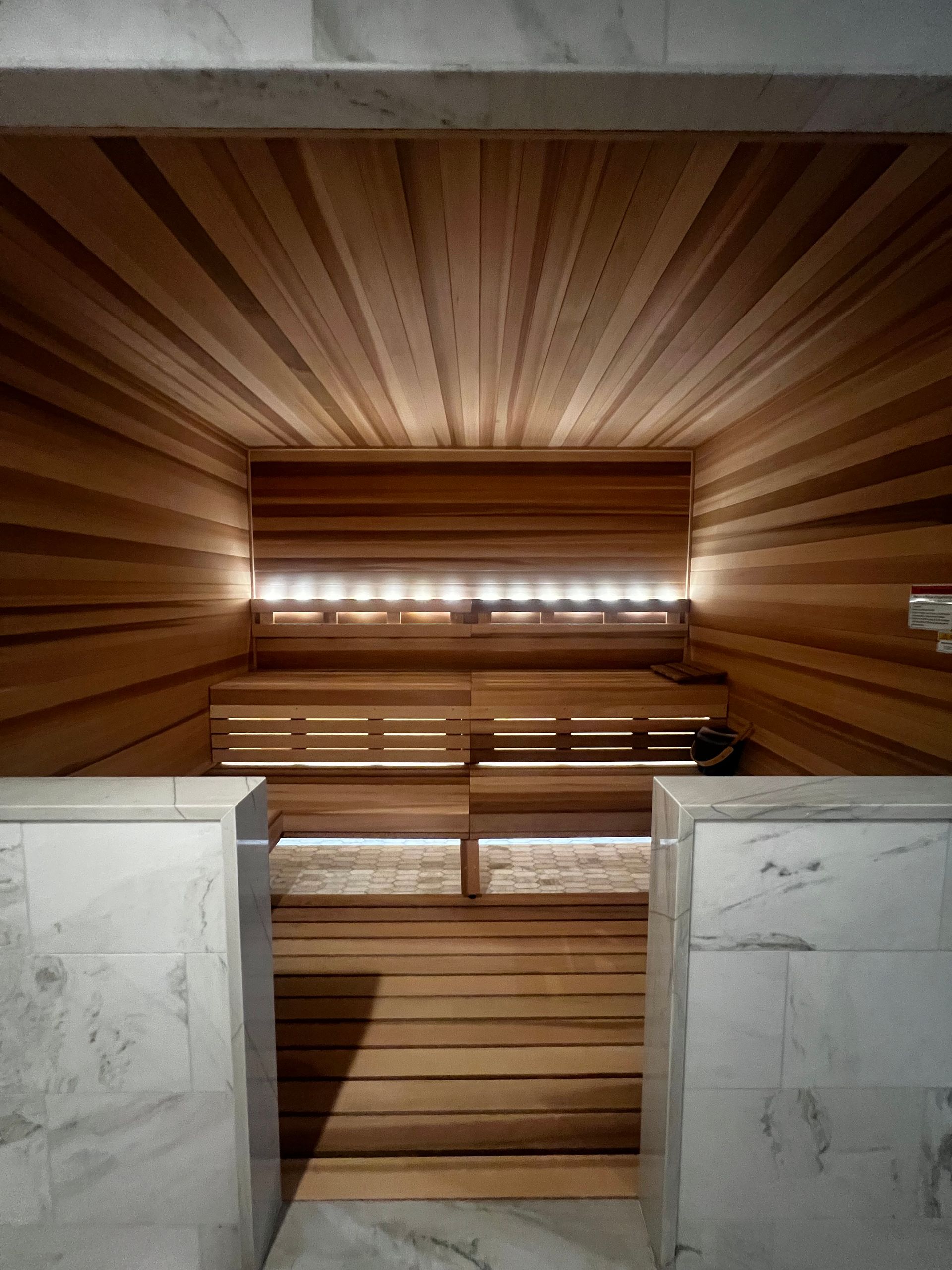 Wood-paneled sauna with wooden benches and warm backlit walls, viewed from the entrance