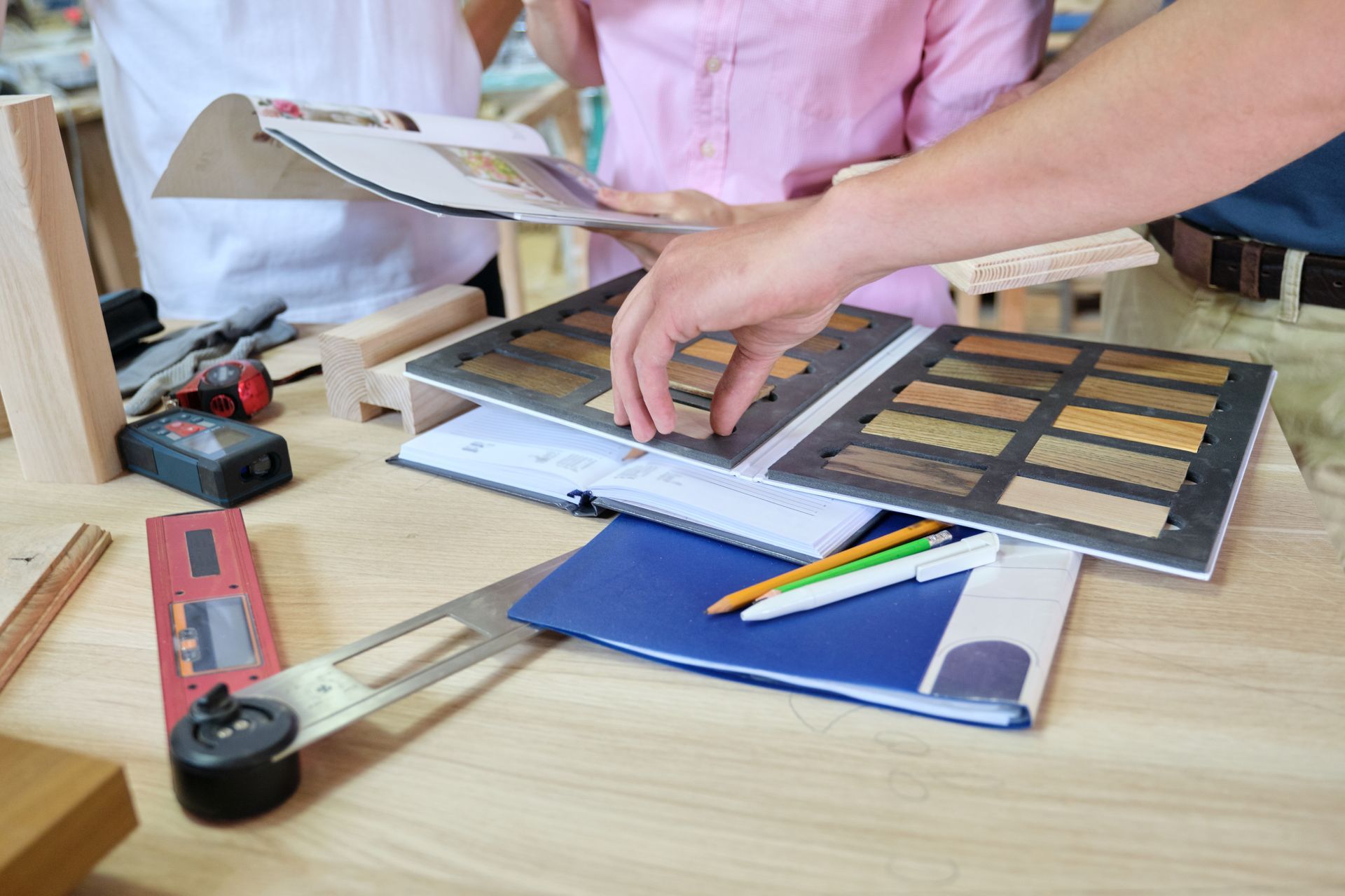 Hands choosing paint swatches and pencils on a wooden desk in a design workspace