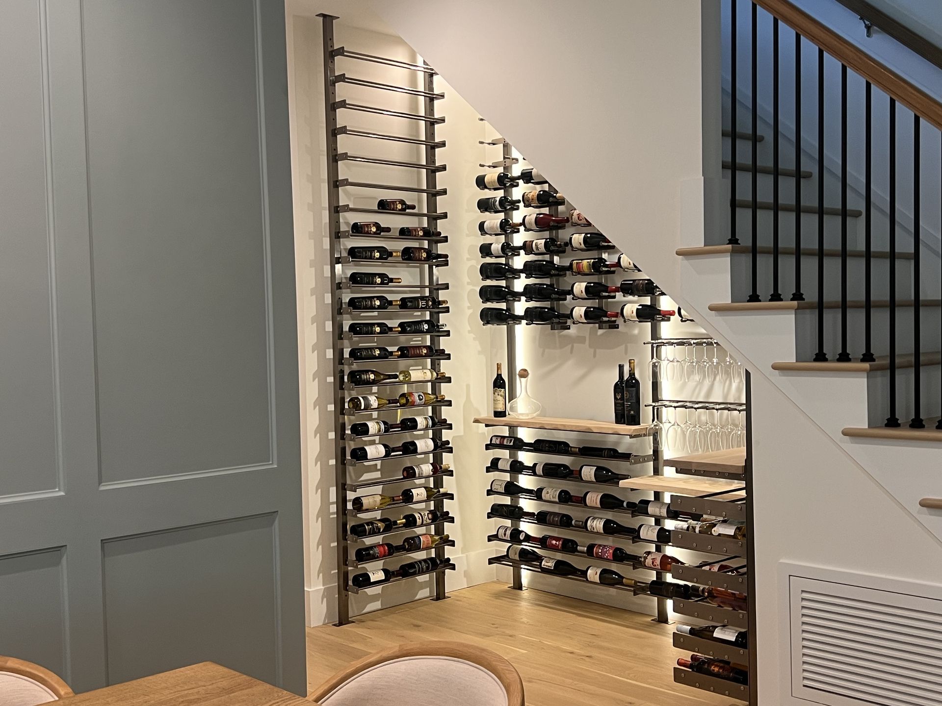 Built-in wine rack display in a home staircase alcove with bottles on wall-mounted shelves