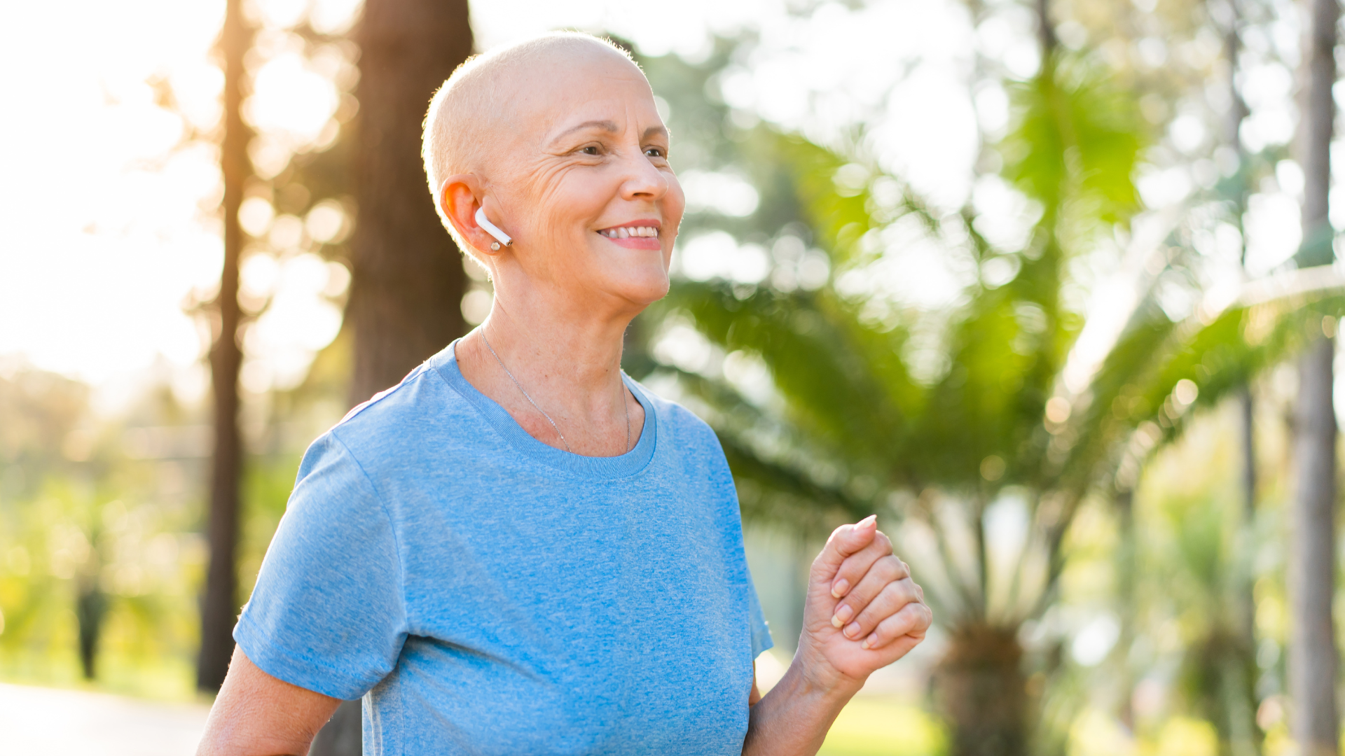 Woman with cancer smiles while jogging outdoors; wearing earbuds and a blue shirt.
