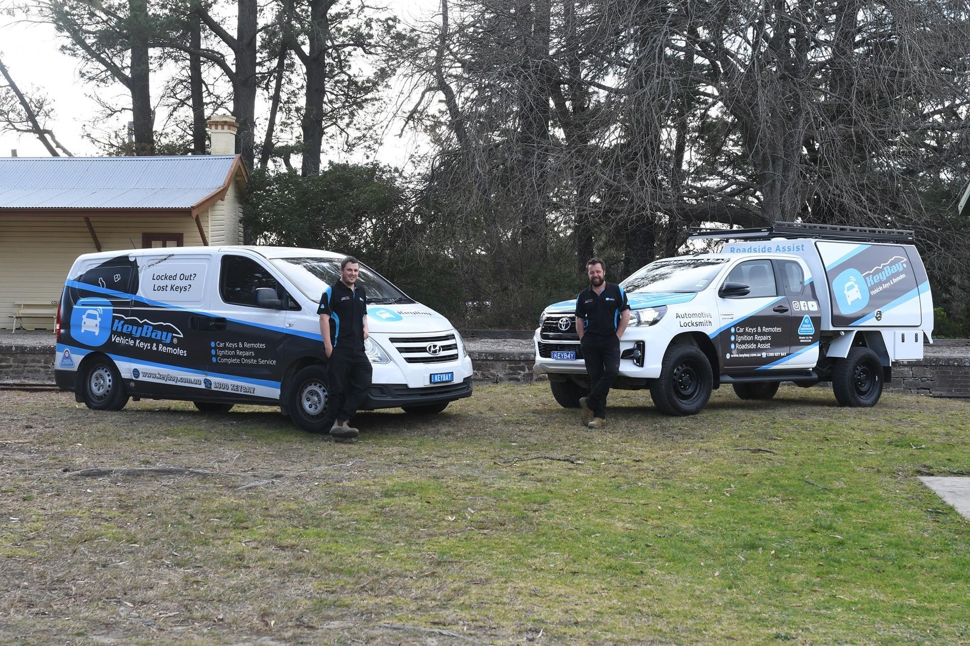 Two service vans with logos parked on grass, with two people standing beside them outdoors — KeyBay in Mittagong, NSW