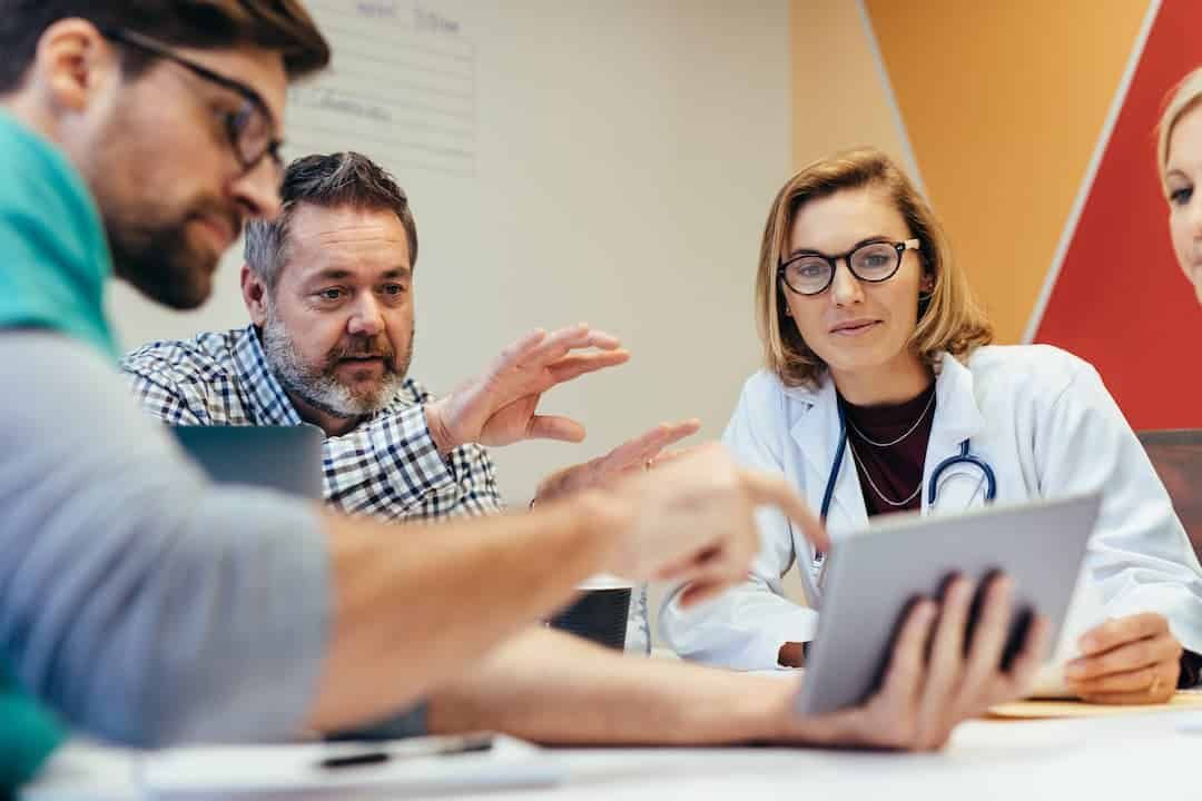 Group of Doctors Are Sitting Around a Table Looking at a Tablet — KeyBay in Berrima, NSW