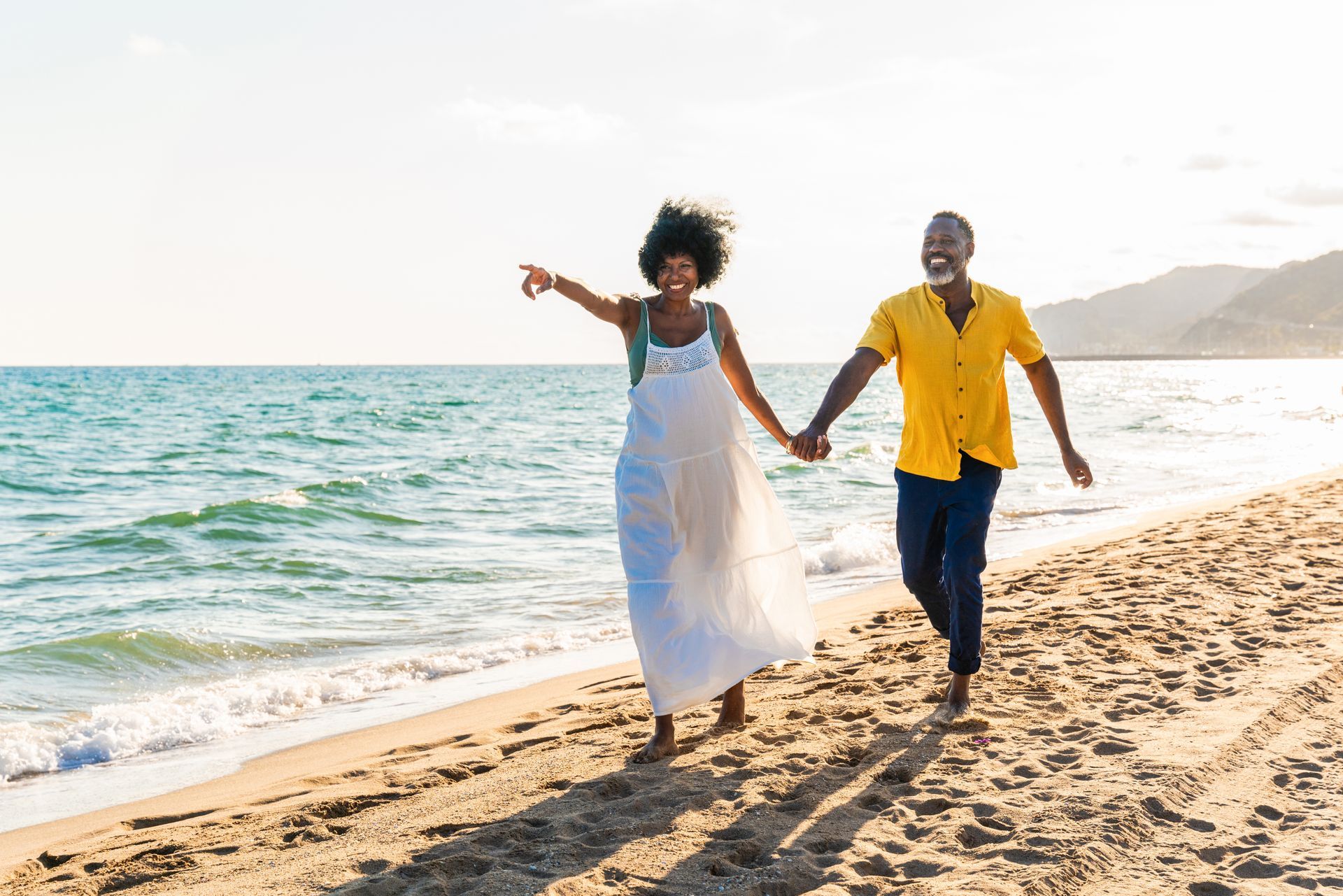 Couple holding hands and walking along a sunny beach near the ocean