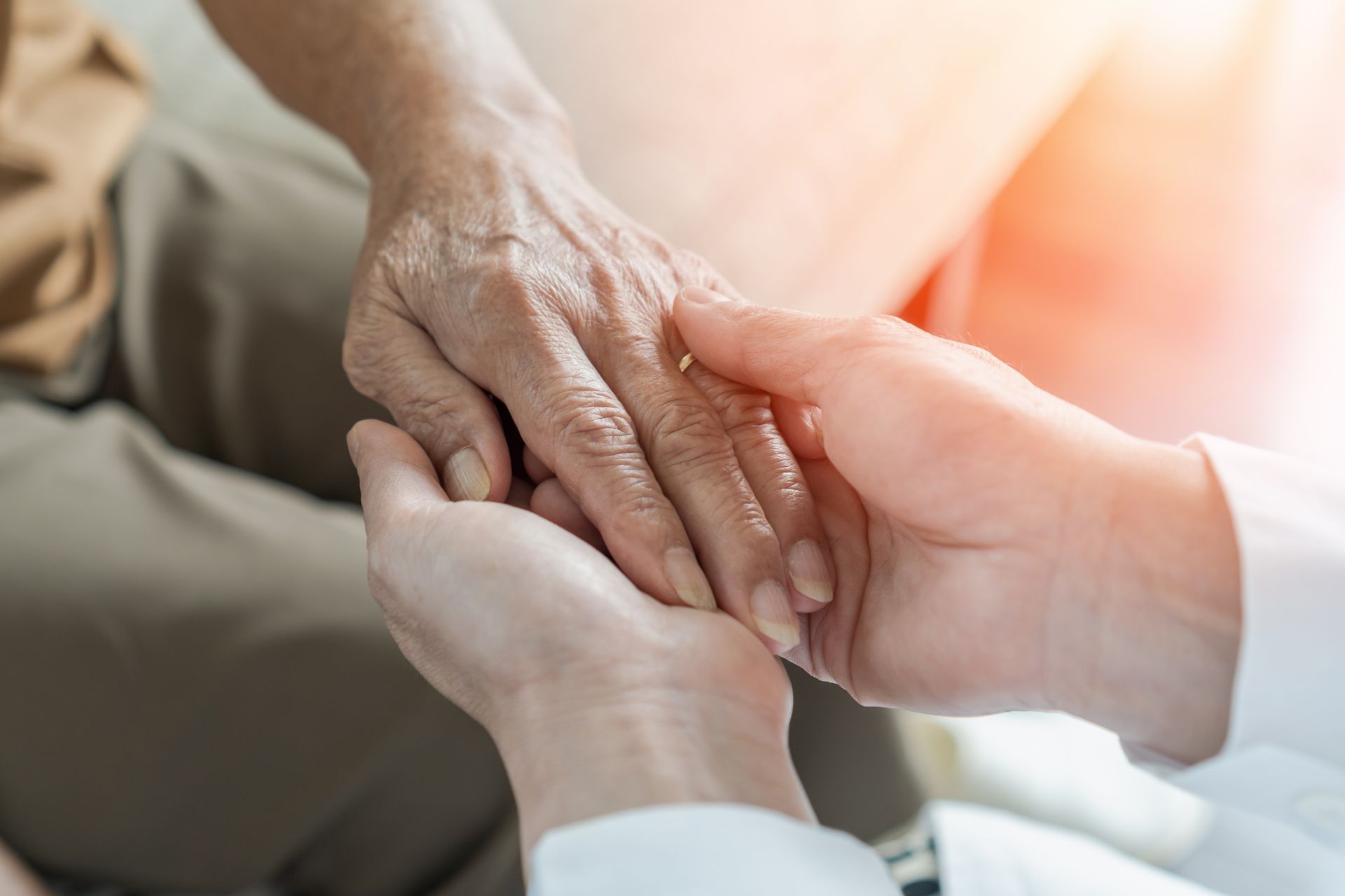 Hands gently holding an older person's hand in a warm, softly lit setting