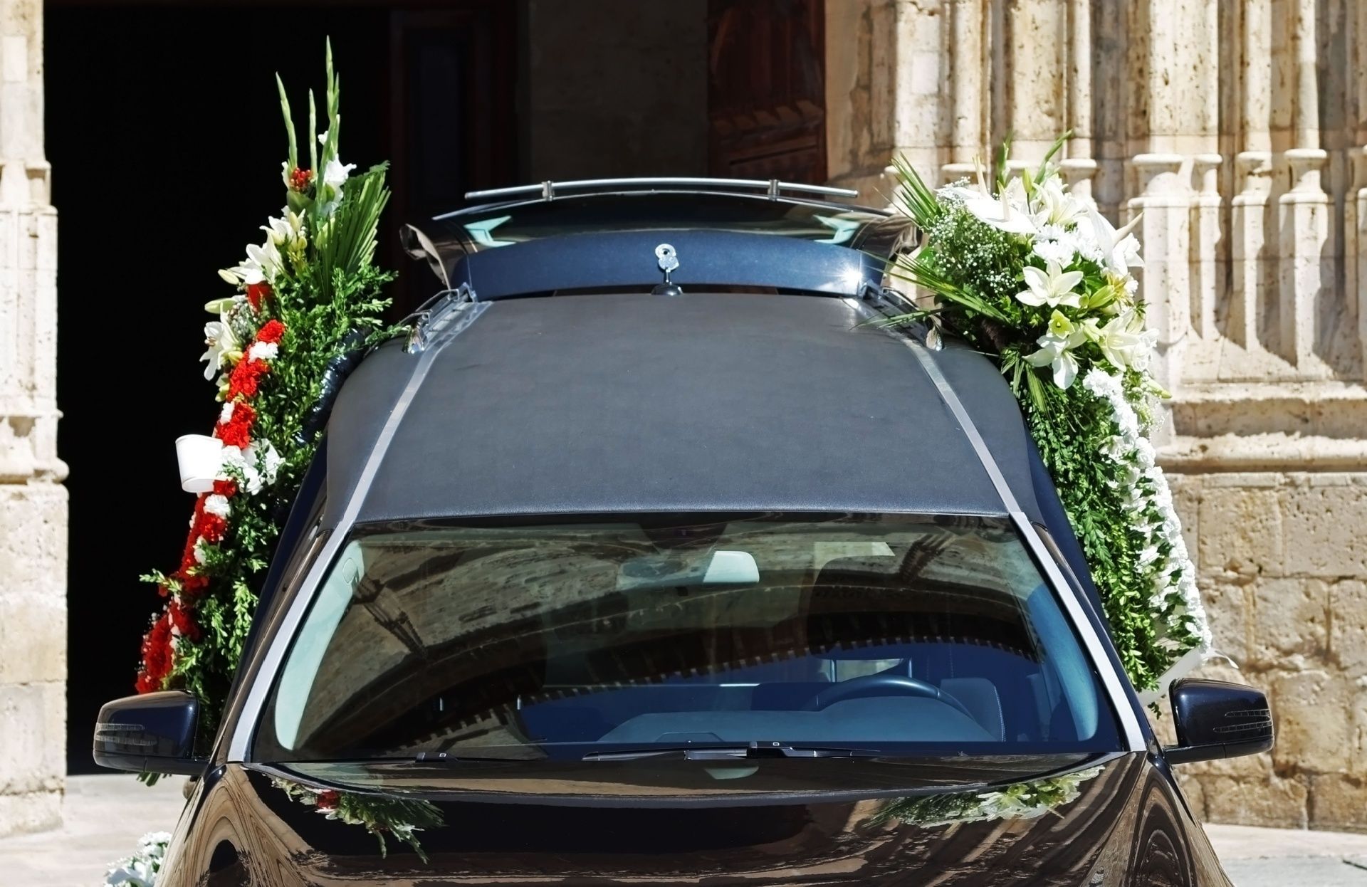 Black hearse with floral arrangements outside a building.