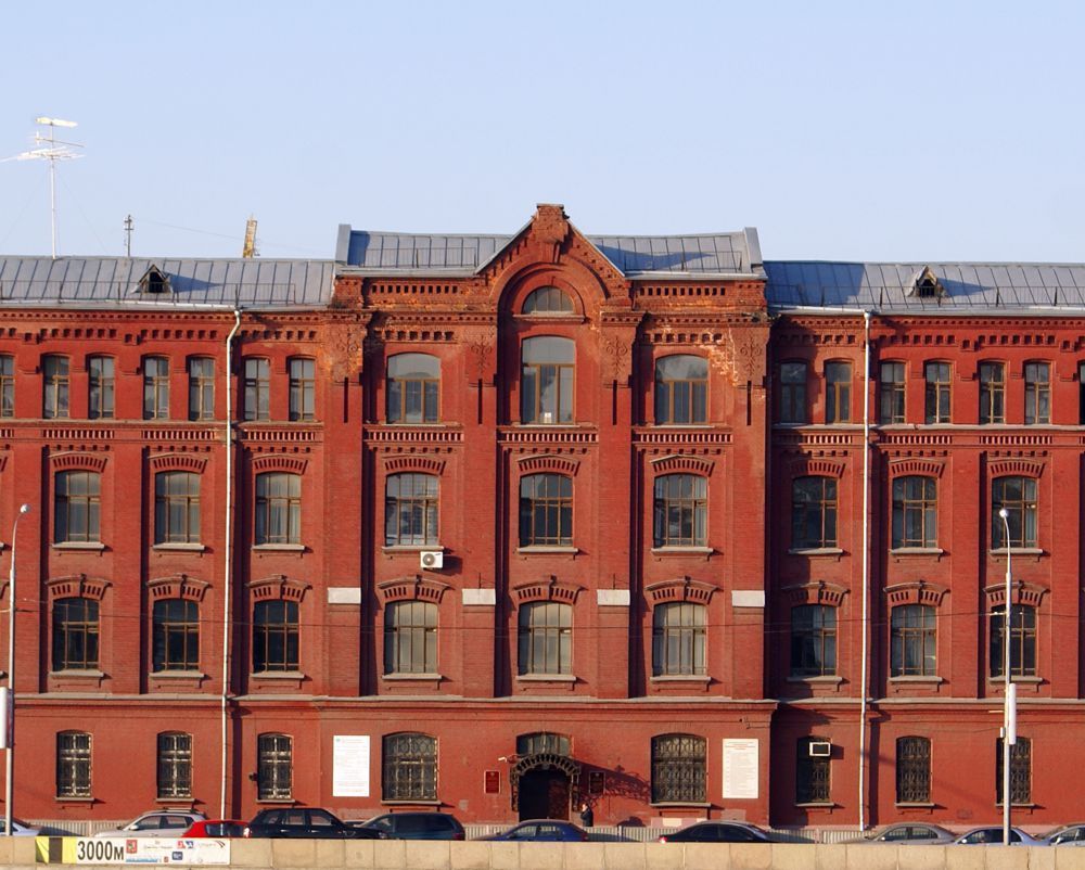 Red-brick Victorian building facade with arched central gable and rows of tall windows under a blue sky