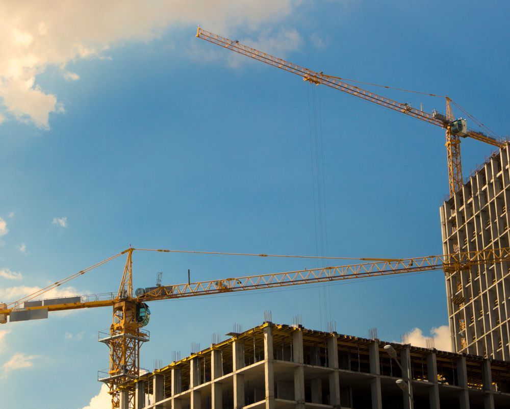 Construction cranes over a building site at sunset, with a partly built structure and blue sky